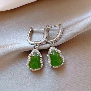 Detail view of green gourd drop earrings with sparkling crystals on silk fabric