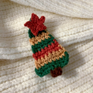 Detailed view of a handmade crochet Christmas tree hair clip on soft white knit fabric