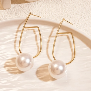 Dettaglio di orecchini geometrici in oro con perle bianche su un vassoio di ceramica