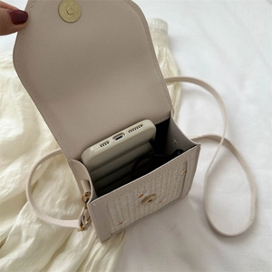 Daisy embroidered straw crossbody bag showing interior capacity with phone and sunglasses