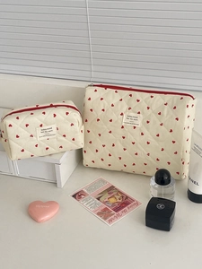 Set of two quilted makeup bags with red heart patterns and zip closure in a cozy desk setting