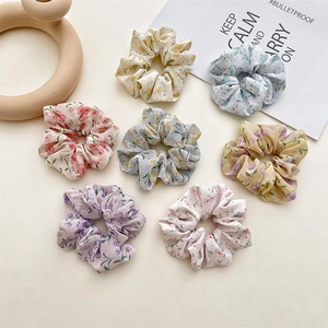 Set of 7 floral chiffon hair scrunchies in various pastel colors on a beige background