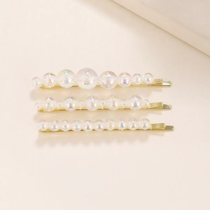 Close-up of golden hair clips with colorful iridescent bubble pearls on beige background