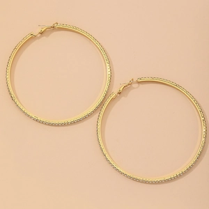 Detailed view of large gold hoop earrings with sparkling rhinestones on beige background