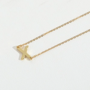 Dettaglio macro di una collana dorata con ciondolo lettera X su pelle bianca