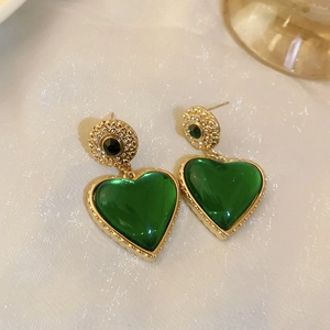 Detail of vintage heart earrings with green gemstone on luxurious white silk backdrop