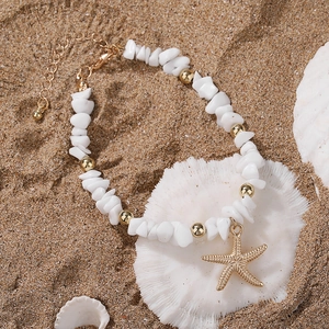 Detailed close-up of a white natural stone anklet with a golden starfish on a sandy beach
