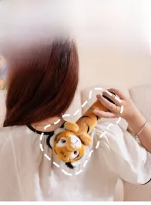 Manual tiger plush massage hammer shown being used on back in a cozy home setting