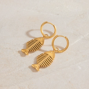 Luxurious gold fishbone drop earrings in stainless steel on a beige stone surface