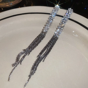 Close-up of silver tassel earrings with inlaid rhinestones on a white ceramic plate