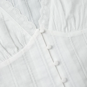 Detail of V-neckline with delicate lace floral trim and covered buttons on white fabric