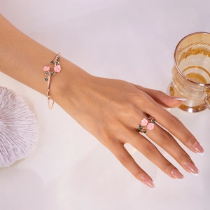 Detailed view of rose gold floral jewelry set with pink enamel on a female model's hand