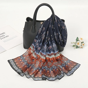 Detail of bohemian chiffon scarf with floral print draped on a black leather handbag