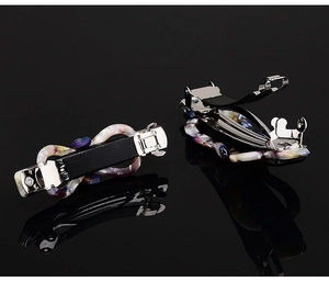 Close-up of marble pattern acetate bow hair clips on a black reflective surface