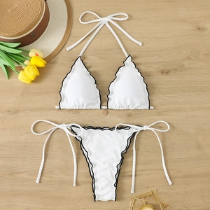 Flat lay of white scalloped halter bikini with black trim and gold charm on wood