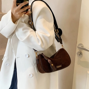 Brown suede crossbody pillow bag with wide shoulder strap shown on a model