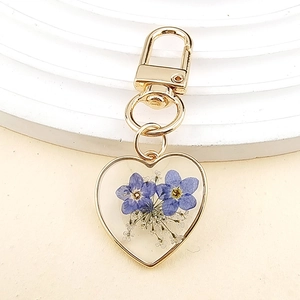 Close-up of heart-shaped gold keychain featuring real blue dried flowers in clear resin
