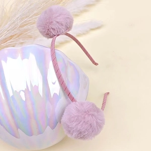 Close-up of cute purple plush pom pom headband placed on a decorative pearl seashell