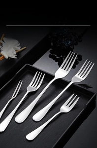 Set of five polished stainless steel forks for steak and dessert on a textured tray