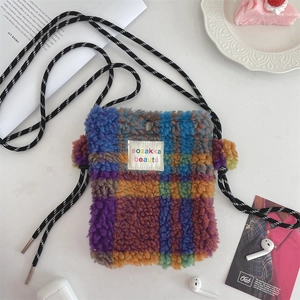 Close-up of a rainbow checkered plush mini shoulder bag with drawstring strap on a desk