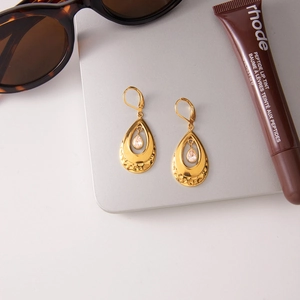 Detailed close-up of golden teardrop earrings with zircon on a stylish matte surface