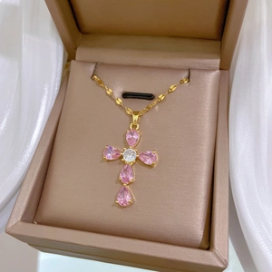 Close-up of golden cross pendant with pink and clear gemstones in a jewelry box