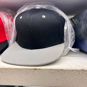 Detail of a two-tone snapback hat with black crown and grey flat brim in protective packaging