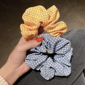 Hand holding yellow and blue polka dot fabric scrunchies with pleated texture for women