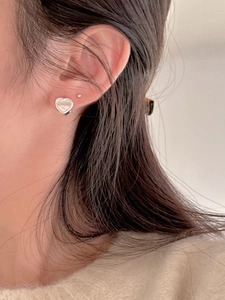 Close-up of minimalist sterling silver heart-shaped earrings on a model's earlobe