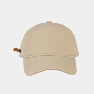 Detail of a beige cotton baseball cap featuring a vintage brown leather patch on the side