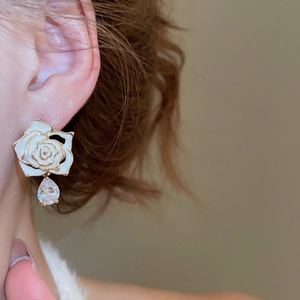 Detail of rose floral earring with white enamel petals and a sparkling zircon teardrop charm
