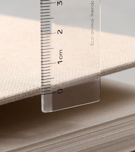 Close-up of beige linen sketchbook cover thickness measured with a clear ruler