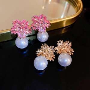 Detailed close-up of diamond-encrusted flower pearl earrings on a dark reflective surface