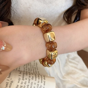 Detailed close-up of acrylic beaded elastic bracelet with amber and gold metallic cubes