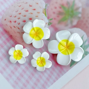 Macro shot of white and yellow resin plumeria flower charms on a strawberry card
