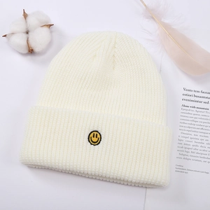 Detalle de textura de punto de gorro crema con bordado de carita sonriente amarilla y algodón