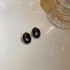 Detailed shot of black enamel earrings featuring a silver hand gesture and orange zircon