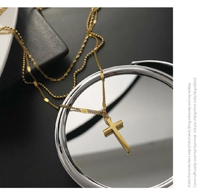 Detailed view of triple-layer gold titanium cross necklace on a reflective mirror surface