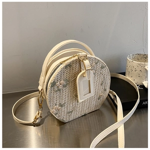 Detail view of round straw crossbody bag with leather trim and metal buckle on metal surface