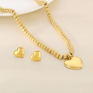 Detailed view of golden bead necklace and matching heart stud earrings on beige fabric