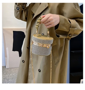 Champagne gold cylindrical bucket bag with rhinestones held by a model in a trench coat