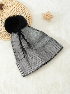 Metallic silver knit beanie with black faux fur pom pom on a white faux fur background