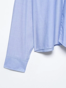 Detail of light blue shirt sleeve and hem showing fine stitching and cotton fabric texture