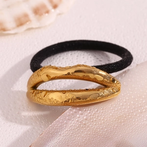 Detail showing a golden lip-shaped metal charm on a black elastic hair tie with water drops