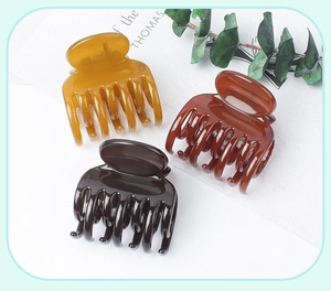 Close-up of three glossy amber and brown hair claws on minimalist prop background