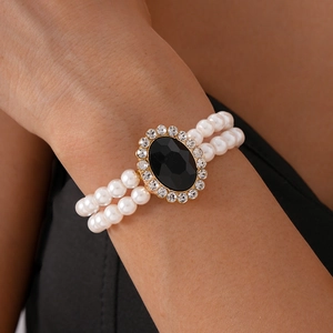 Detail of a double-strand pearl bracelet with a faceted black oval gemstone and gold rim