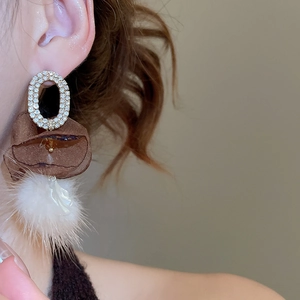 Close-up of model wearing oval rhinestone drop earrings with mesh petals and white fur balls