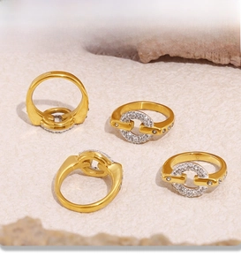 Close-up of four 18k gold plated PVD rings with shimmering zircons on textured stone surface