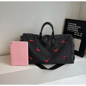 Detailed view of black travel bag with cherry embroidery and pink tablet for size reference
