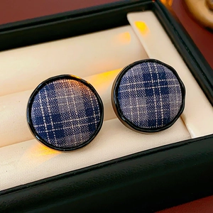 Macro shot of blue plaid fabric round stud earrings inside a jewelry box